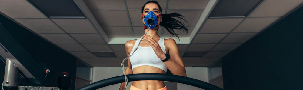 Fit young woman running on a treadmill with a respirator on, completing a VO2 max test Fit young woman running on a treadmill with a respirator on, completing a VO2 max test